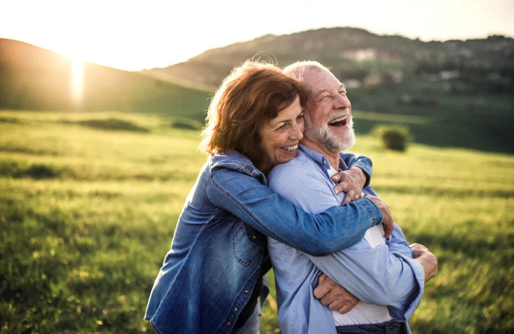 Side view of senior couple hugging outside in spring nature at sunset.