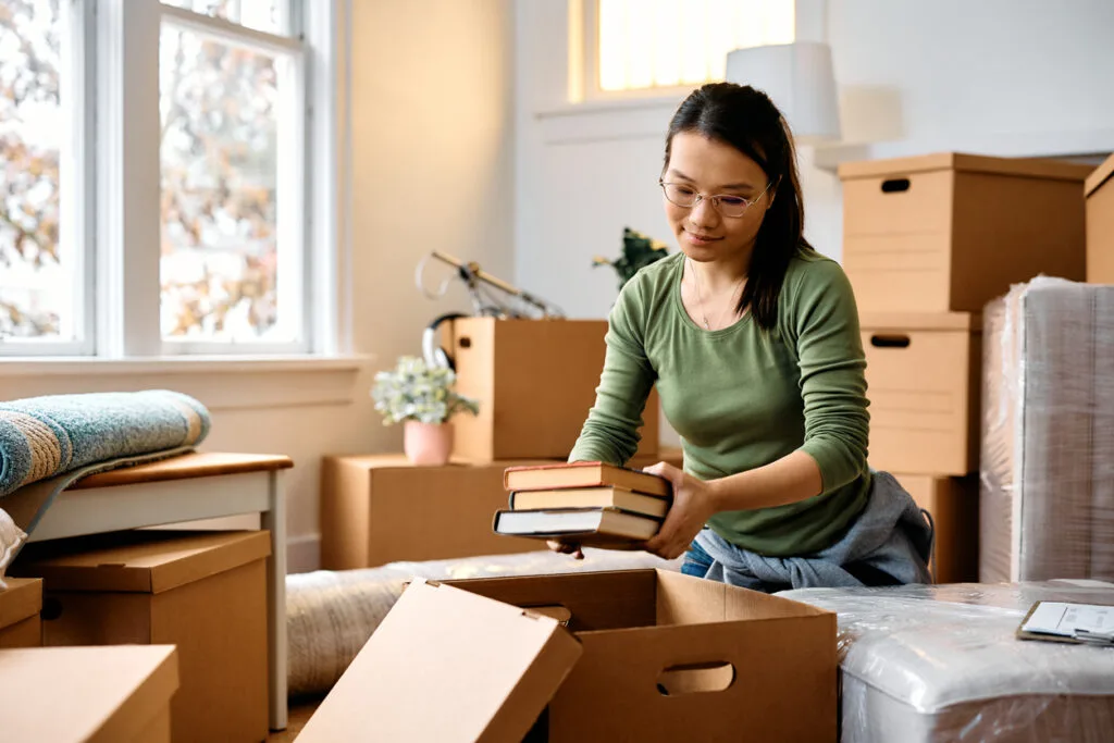 Young Asian woman unpacking cardboard boxes while moving into a new home.